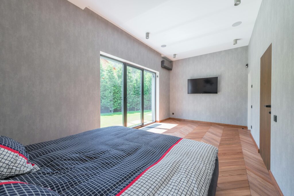 pexels-photo-7587855-7587855 Bright and cozy minimalist bedroom with large sliding glass doors and wooden flooring.